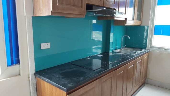 Kính ốp bếp màu xanh ngọc kết hợp với tủ gỗ làm nổi bật không gian bếp